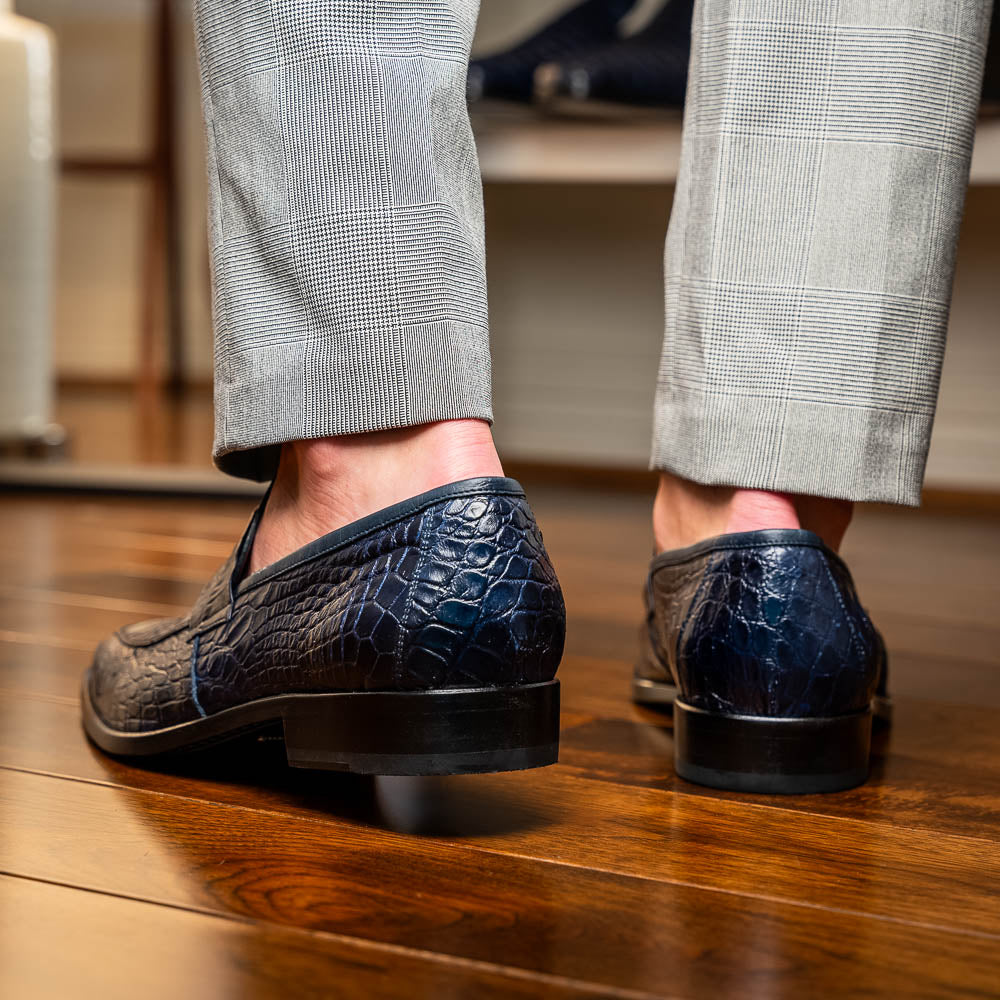 A pair of Matteo Navy loafers by Marco Di Milano, crafted in crocodile-pattern navy leather with a penny strap, red interior lining, and black soles; one shoe props against the other to reveal the sole.