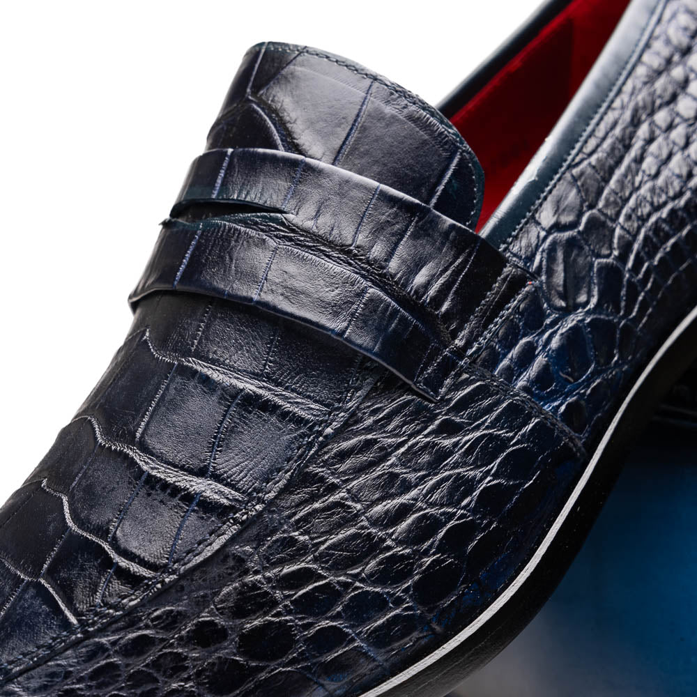 A pair of Matteo Navy loafers by Marco Di Milano, crafted in crocodile-pattern navy leather with a penny strap, red interior lining, and black soles; one shoe props against the other to reveal the sole.