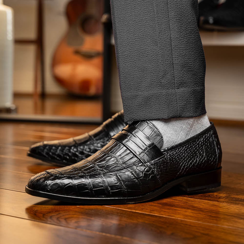 The Matteo Black by Marco Di Milano is a pair of black genuine alligator slip-on shoes with a polished brown leather sole, embossed branding, and hand-painted finishes, shown against a white background.