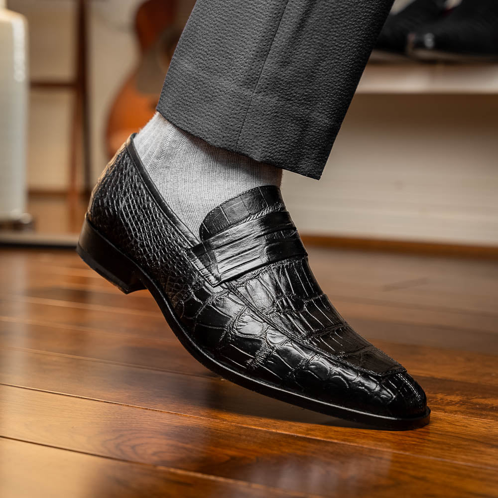 The Matteo Black by Marco Di Milano is a pair of black genuine alligator slip-on shoes with a polished brown leather sole, embossed branding, and hand-painted finishes, shown against a white background.