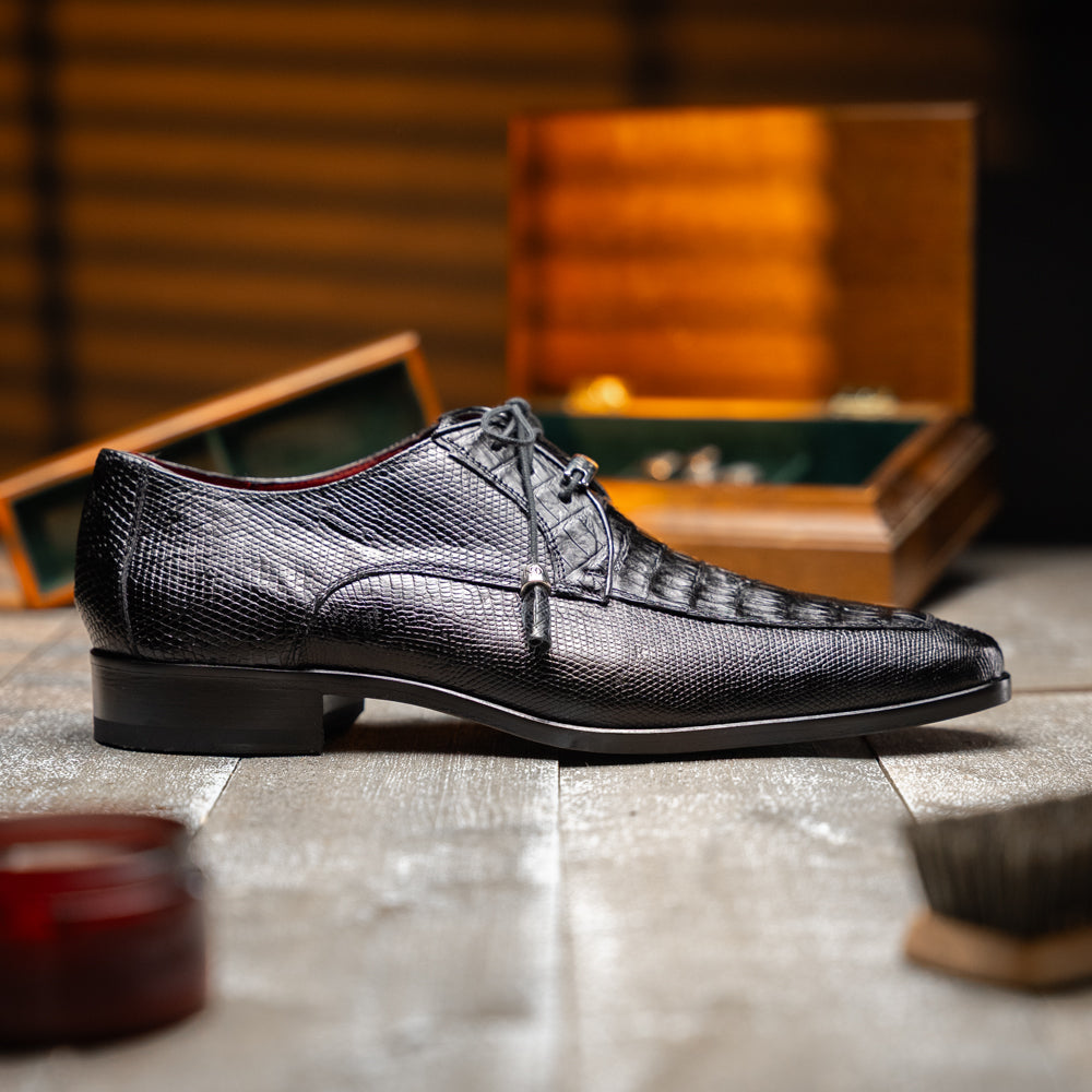 A pair of Merida Black dress derby shoes by Marco Di Milano, crafted from textured black leather caiman—one upright and one on its side revealing the brown sole stamped with the brand’s logo—an unmistakable statement in luxury footwear.