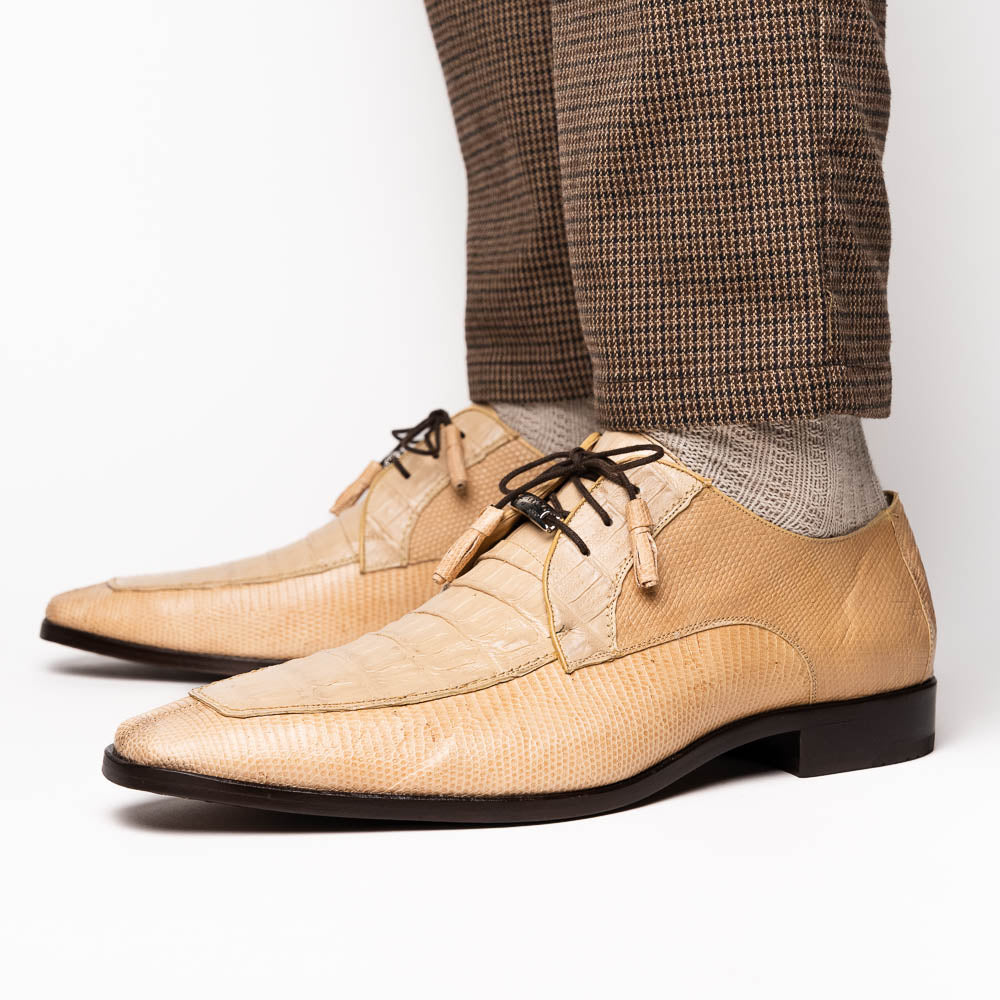 A pair of beige Merida Orix dress derby shoes by Marco Di Milano with black laces, one upright and one leaning to reveal the branded sole—a striking statement in luxury footwear.
