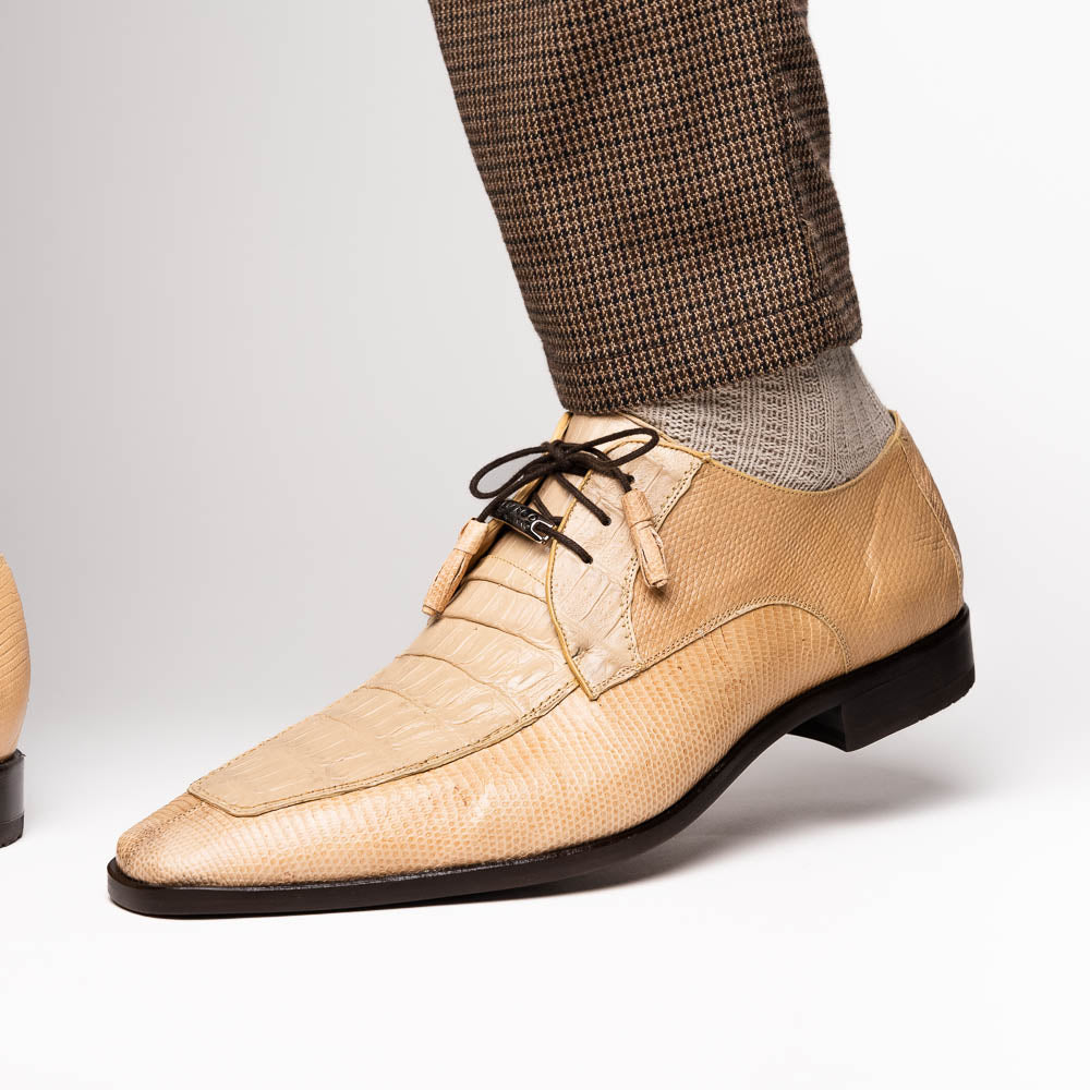 A pair of beige Merida Orix dress derby shoes by Marco Di Milano with black laces, one upright and one leaning to reveal the branded sole—a striking statement in luxury footwear.