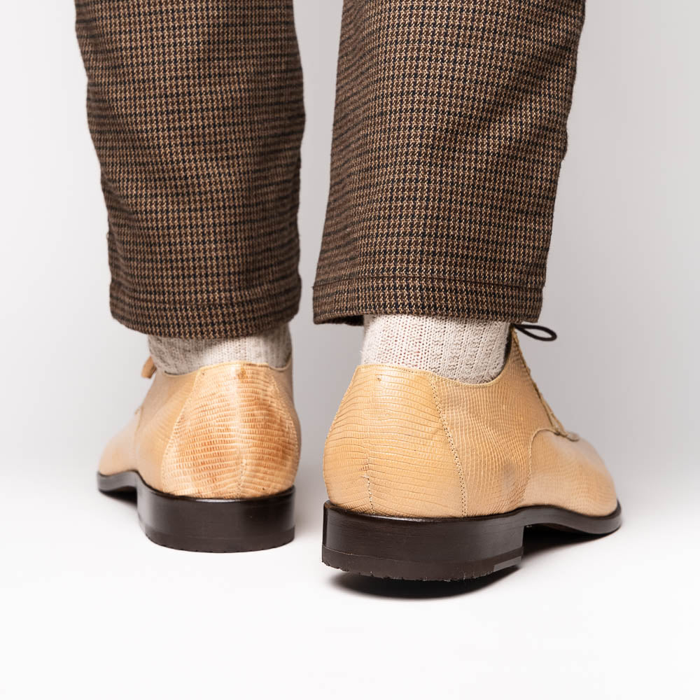 A pair of beige Merida Orix dress derby shoes by Marco Di Milano with black laces, one upright and one leaning to reveal the branded sole—a striking statement in luxury footwear.