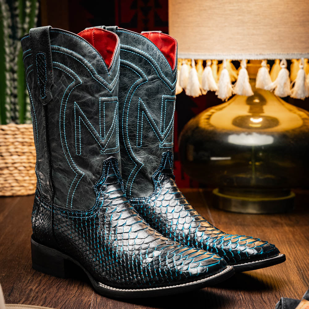 The Missouri Black / Blue boots by Marco Di Milano are handcrafted men's cowboy boots in black and blue, featuring genuine python skin and a textured snakeskin pattern—one boot upright, the other revealing the branded sole.