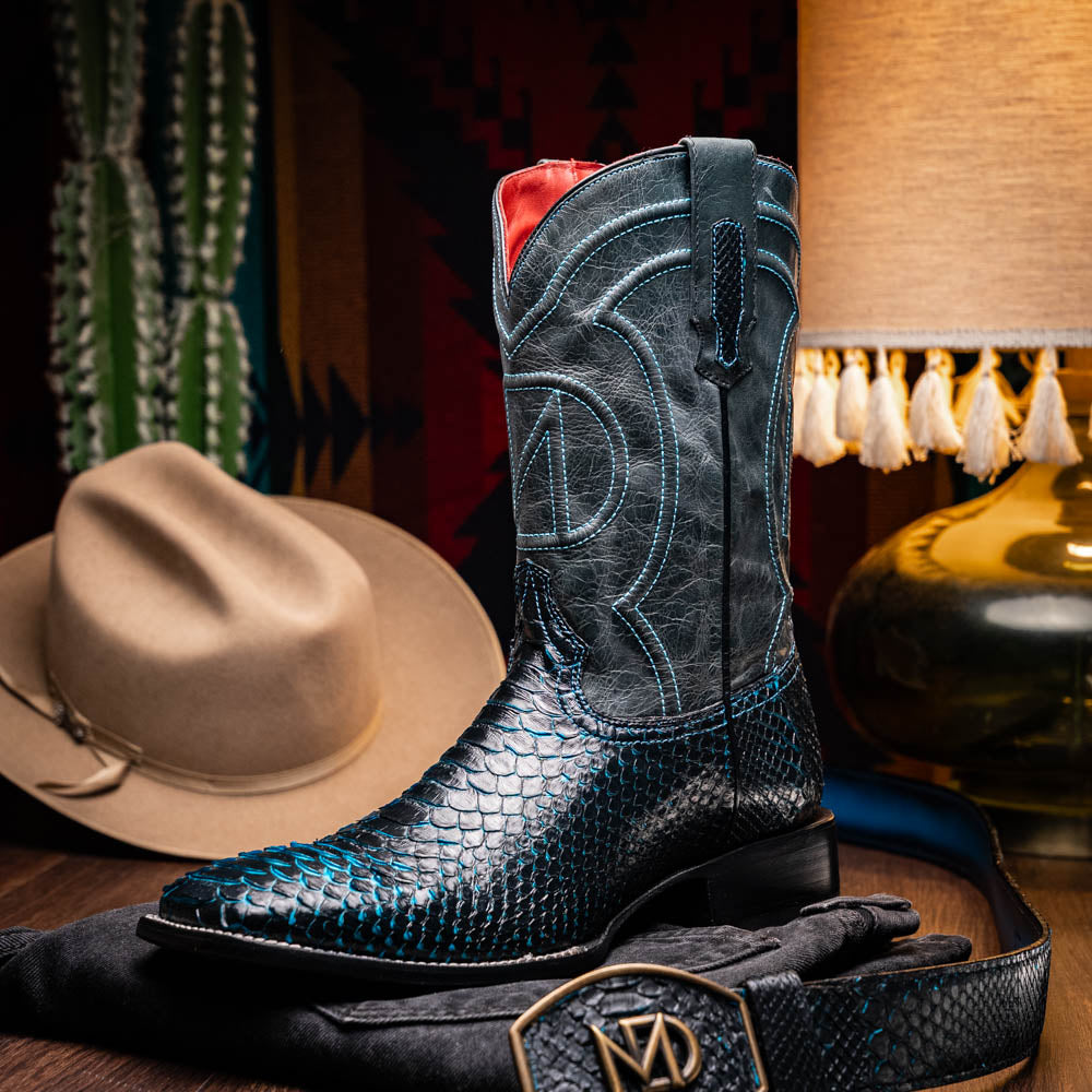 The Missouri Black / Blue boots by Marco Di Milano are handcrafted men's cowboy boots in black and blue, featuring genuine python skin and a textured snakeskin pattern—one boot upright, the other revealing the branded sole.