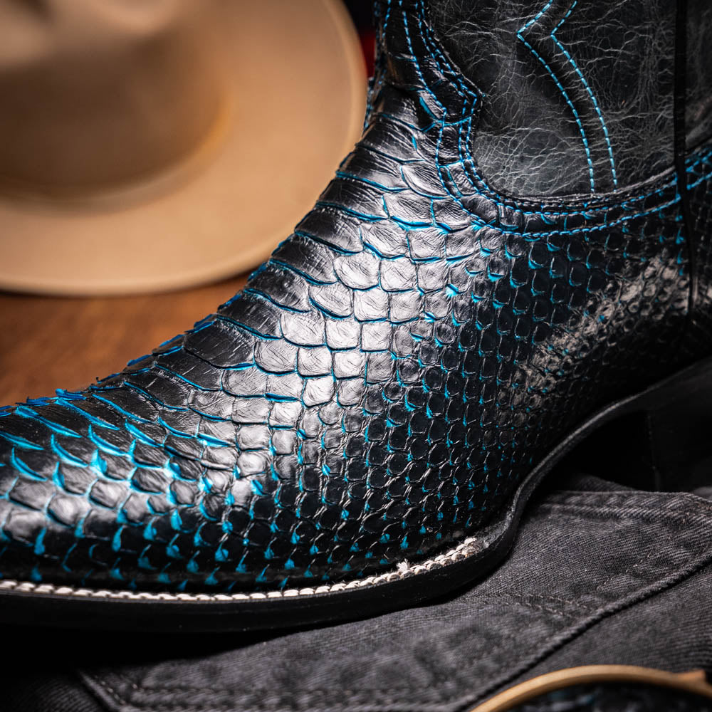 The Missouri Black / Blue boots by Marco Di Milano are handcrafted men's cowboy boots in black and blue, featuring genuine python skin and a textured snakeskin pattern—one boot upright, the other revealing the branded sole.
