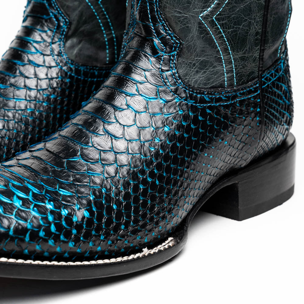 The Missouri Black / Blue boots by Marco Di Milano are handcrafted men's cowboy boots in black and blue, featuring genuine python skin and a textured snakeskin pattern—one boot upright, the other revealing the branded sole.