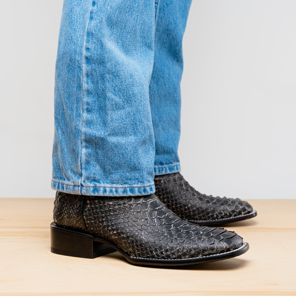 A pair of Missouri Stone White cowboy boots by Marco Di Milano, handcrafted in black textured python leather with branded soles, displayed on a white background.