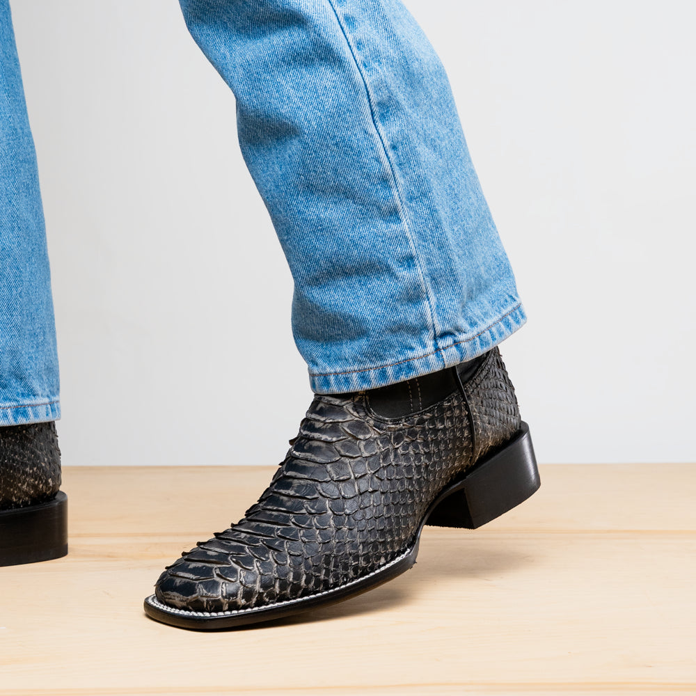 A pair of Missouri Stone White cowboy boots by Marco Di Milano, handcrafted in black textured python leather with branded soles, displayed on a white background.