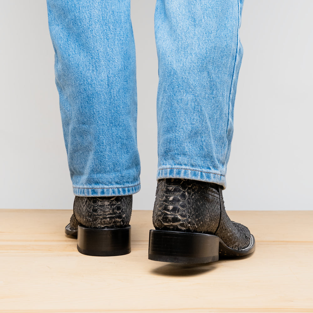 A pair of Missouri Stone White cowboy boots by Marco Di Milano, handcrafted in black textured python leather with branded soles, displayed on a white background.