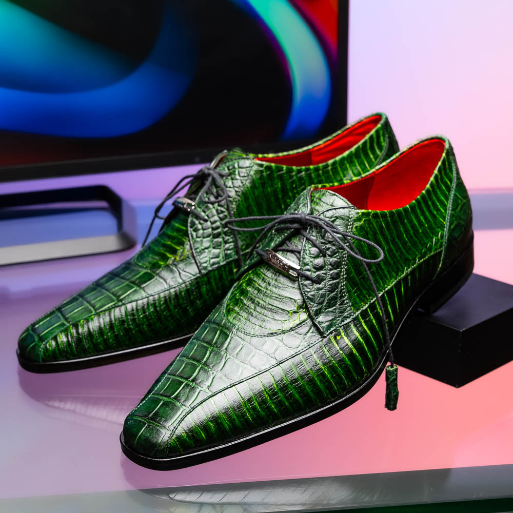 A pair of Moncalieri Green luxury shoes by Marco Di Milano, one upright with tied laces and the other on its side showing the sole—crocodile-patterned elegance at its finest.
