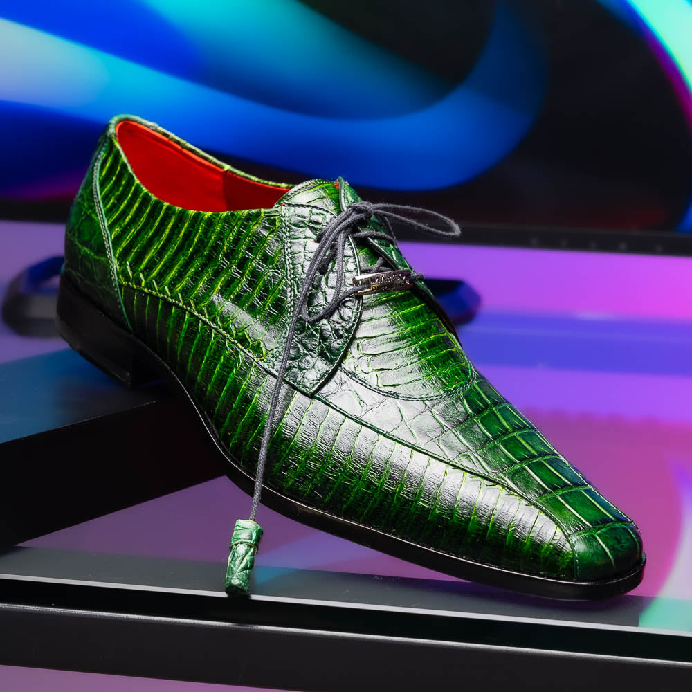 A pair of Moncalieri Green luxury shoes by Marco Di Milano, one upright with tied laces and the other on its side showing the sole—crocodile-patterned elegance at its finest.