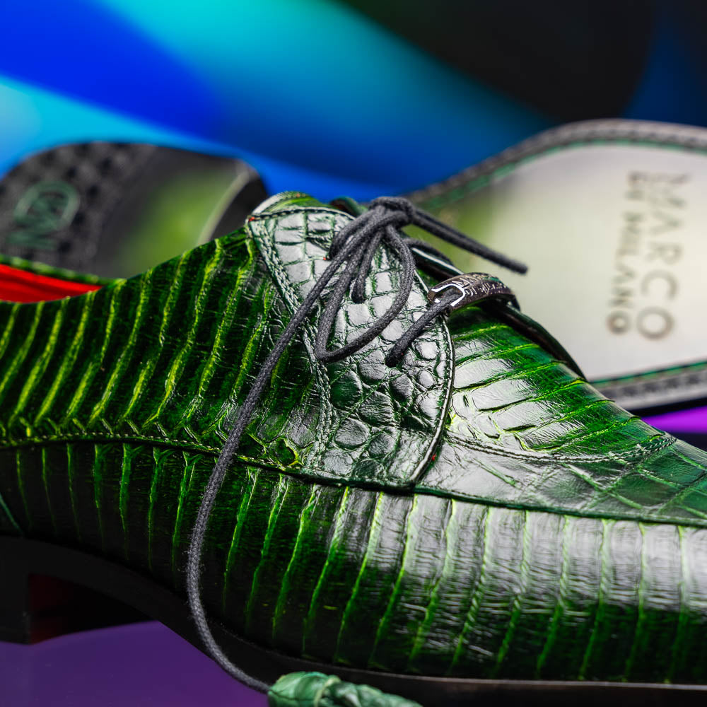 A pair of Moncalieri Green luxury shoes by Marco Di Milano, one upright with tied laces and the other on its side showing the sole—crocodile-patterned elegance at its finest.