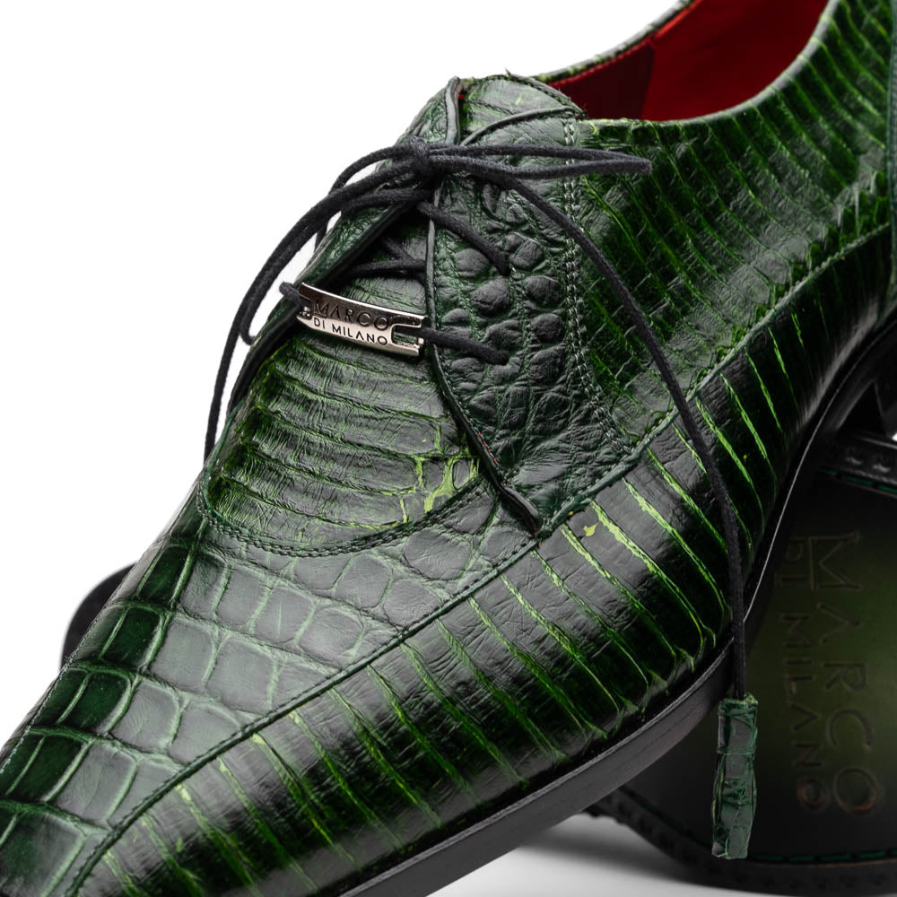A pair of Moncalieri Green luxury shoes by Marco Di Milano, one upright with tied laces and the other on its side showing the sole—crocodile-patterned elegance at its finest.