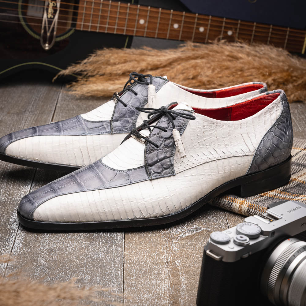 The Marco Di Milano Moncalieri Gray / White men's dress shoes feature a luxury white and grey crocodile pattern, black laces, and black soles, with one shoe stylishly propped against the other.