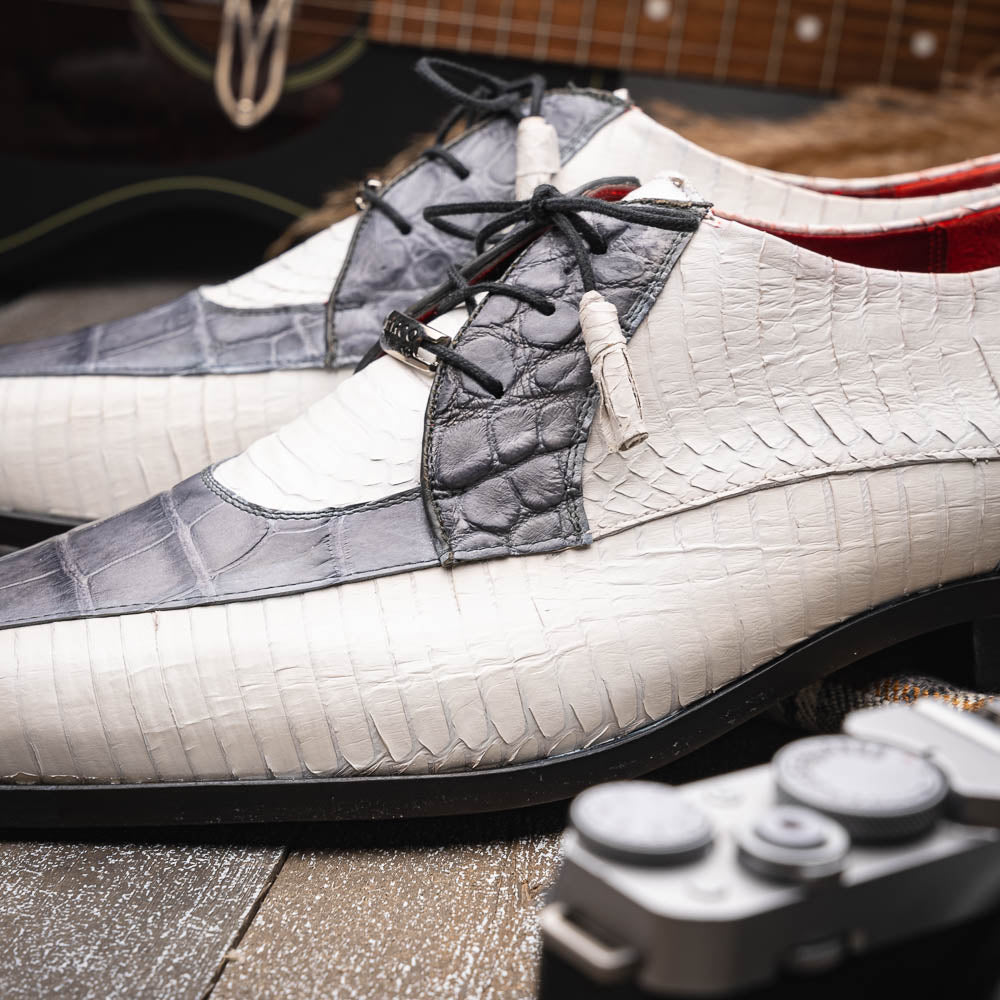 The Marco Di Milano Moncalieri Gray / White men's dress shoes feature a luxury white and grey crocodile pattern, black laces, and black soles, with one shoe stylishly propped against the other.