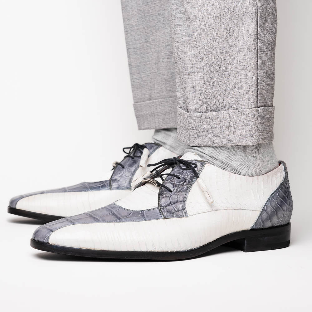 The Marco Di Milano Moncalieri Gray / White men's dress shoes feature a luxury white and grey crocodile pattern, black laces, and black soles, with one shoe stylishly propped against the other.
