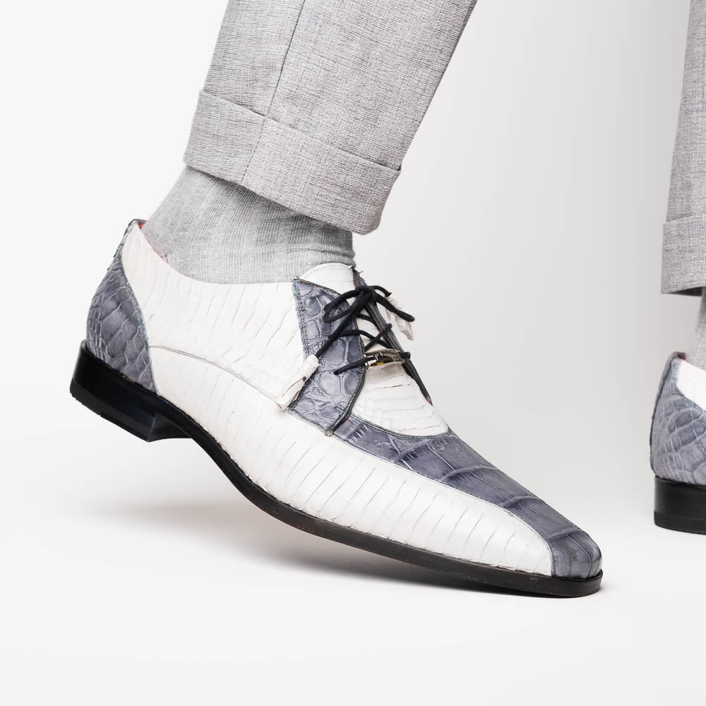 The Marco Di Milano Moncalieri Gray / White men's dress shoes feature a luxury white and grey crocodile pattern, black laces, and black soles, with one shoe stylishly propped against the other.