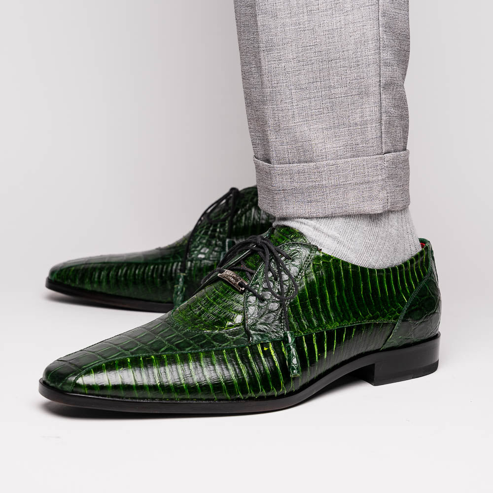 A pair of Moncalieri Green luxury shoes by Marco Di Milano, one upright with tied laces and the other on its side showing the sole—crocodile-patterned elegance at its finest.