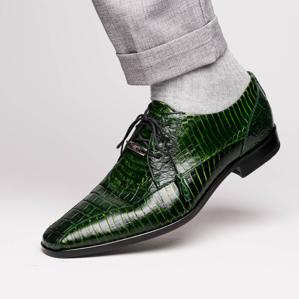 A pair of Moncalieri Green luxury shoes by Marco Di Milano, one upright with tied laces and the other on its side showing the sole—crocodile-patterned elegance at its finest.