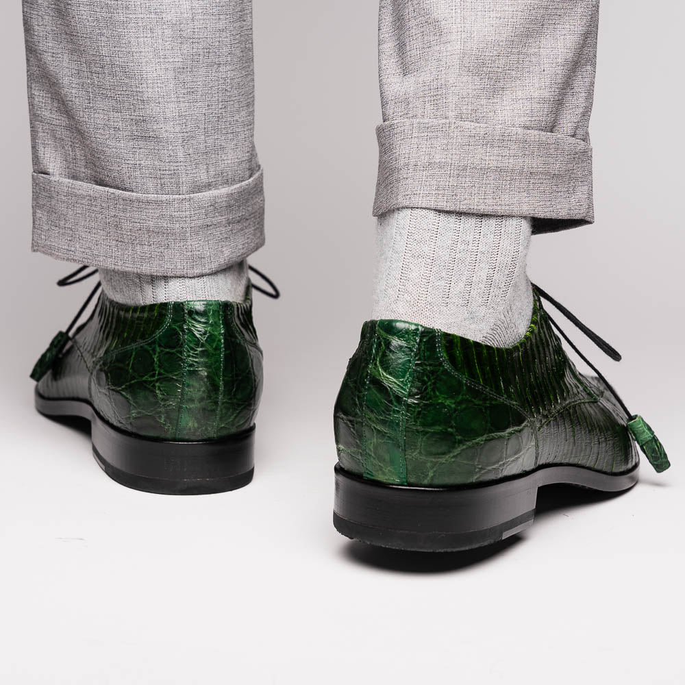 A pair of Moncalieri Green luxury shoes by Marco Di Milano, one upright with tied laces and the other on its side showing the sole—crocodile-patterned elegance at its finest.