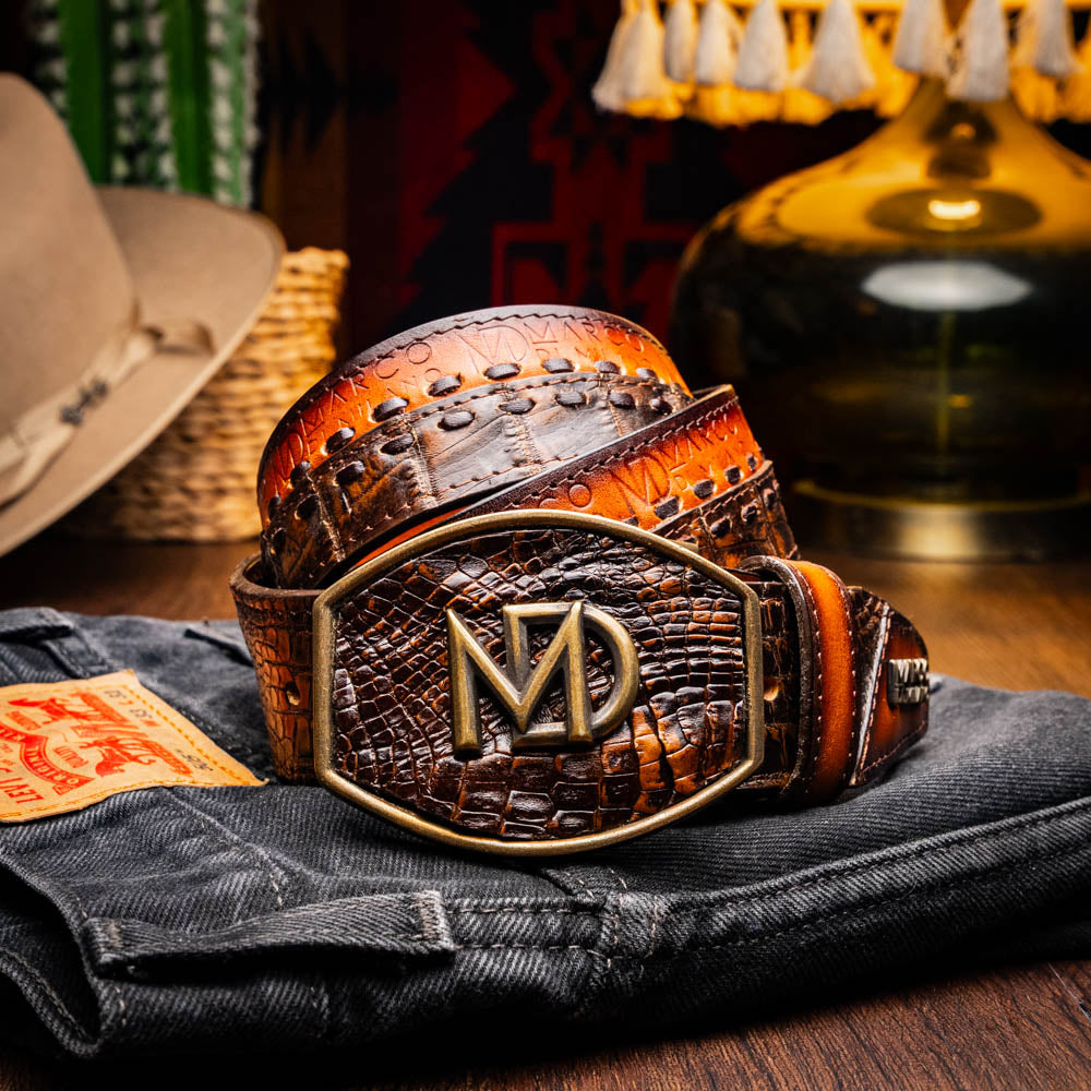 The Montana Belt Aged Brown by Marco Di Milano features aged brown leather with embossed patterns, metal studs, a bold gold MD monogram buckle, and the brand name on the strap for a sophisticated Western look.