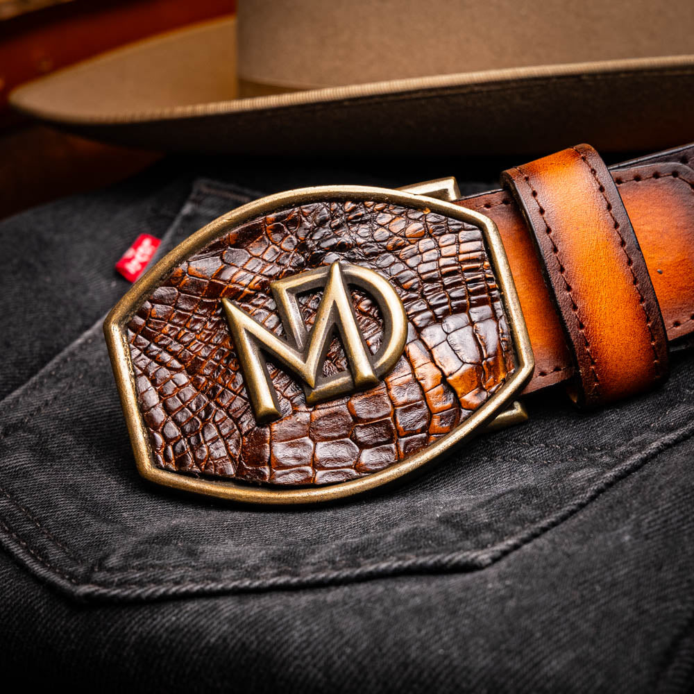 The Montana Belt Aged Brown by Marco Di Milano features aged brown leather with embossed patterns, metal studs, a bold gold MD monogram buckle, and the brand name on the strap for a sophisticated Western look.