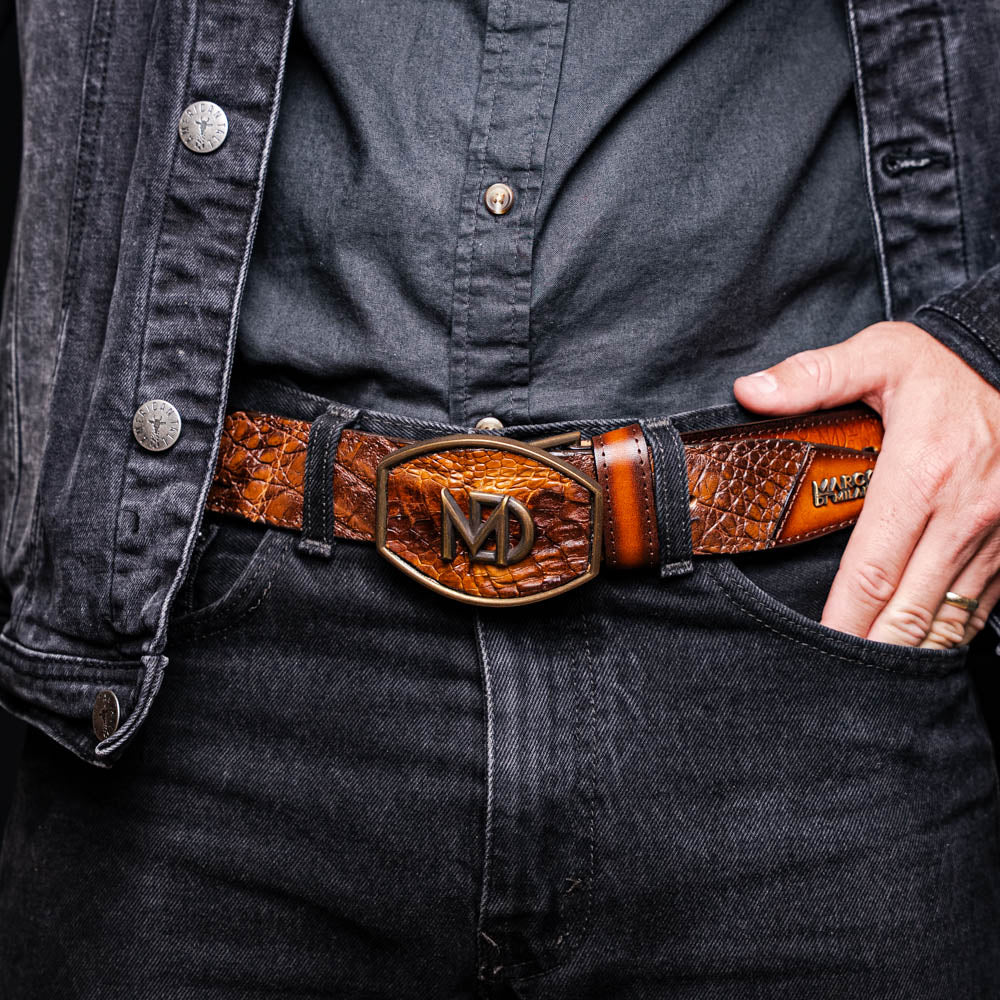 The Montana Belt Aged Maple by Marco Di Milano, featuring stitched details and a large gold MD monogram buckle with embossed branding, is coiled against a white background.