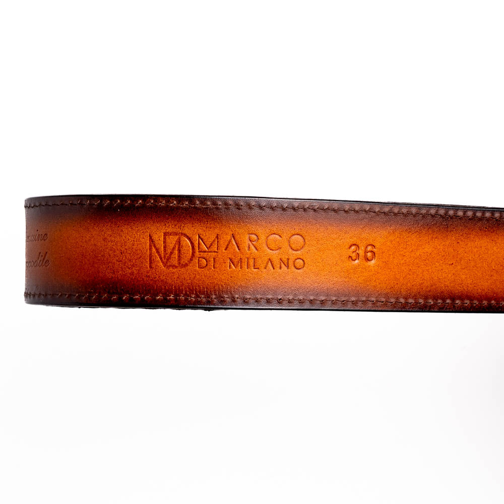 The Montana Belt Aged Maple by Marco Di Milano, featuring stitched details and a large gold MD monogram buckle with embossed branding, is coiled against a white background.