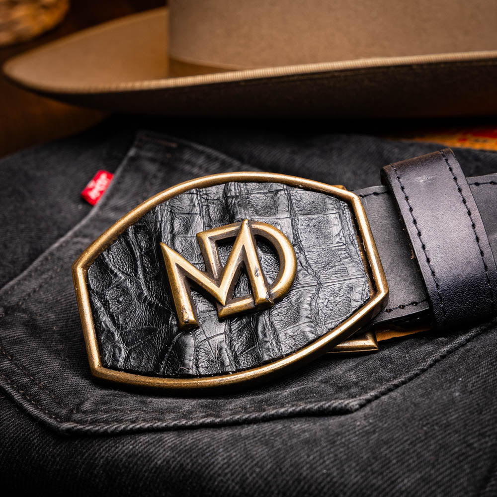 The Marco Di Milano Montana Belt Black features handcrafted black textured leather and a large gold MD monogram buckle, elegantly coiled against a white background.