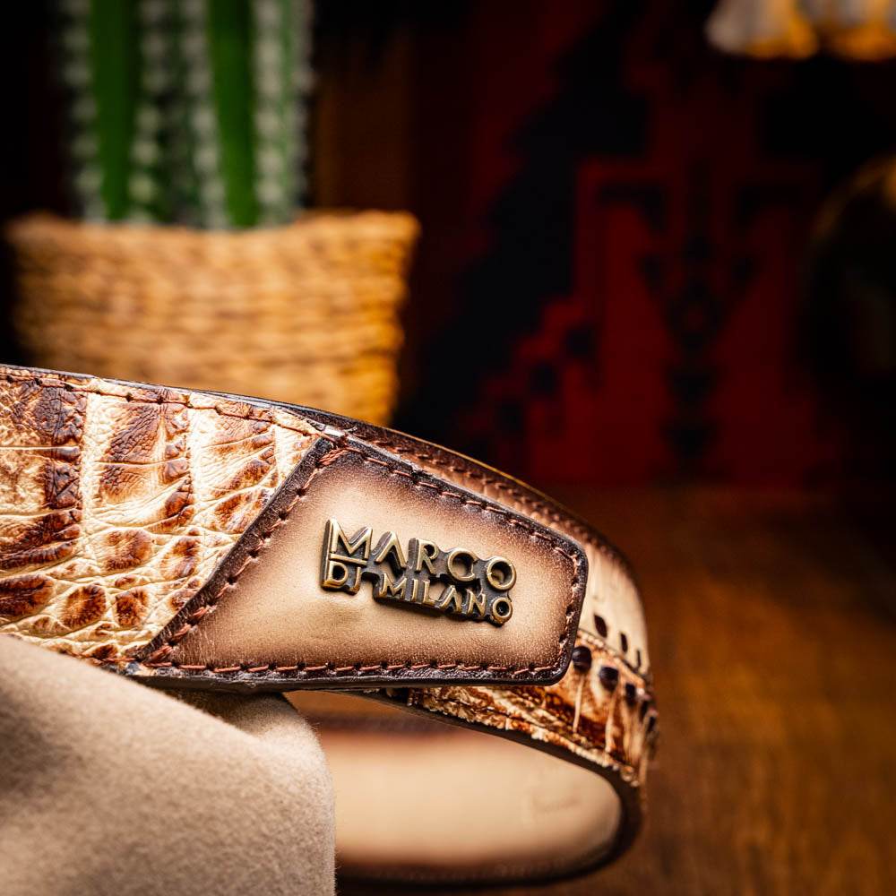 The Montana Belt Stone Orix by Marco Di Milano is a brown handcrafted leather belt with a caiman crocodile pattern and a bold gold MD monogram buckle, elegantly coiled on a white background.