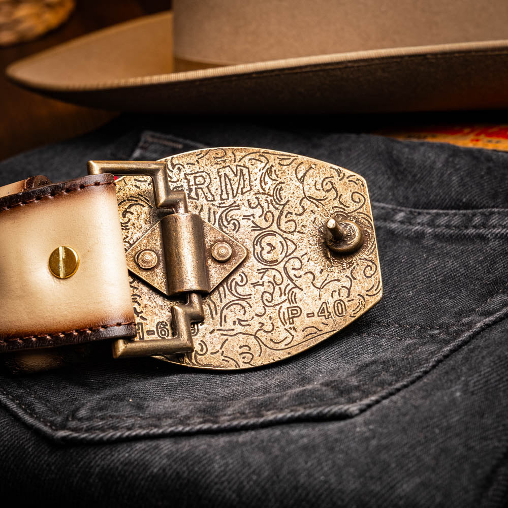 The Montana Belt Stone Orix by Marco Di Milano is a brown handcrafted leather belt with a caiman crocodile pattern and a bold gold MD monogram buckle, elegantly coiled on a white background.