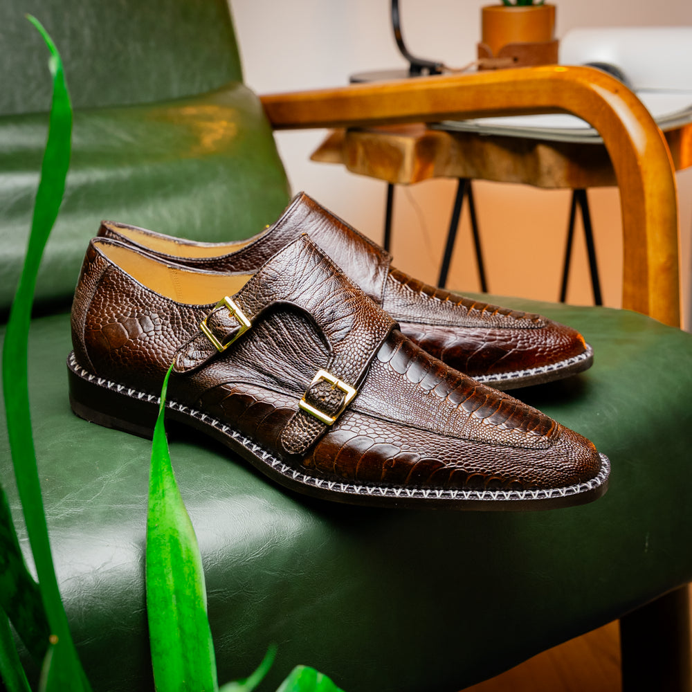 The Marco Di Milano Napoli Brown features brown leather double monk strap dress shoes with a genuine ostrich leg pattern and gold buckles, shown with one shoe upright and the other on its side.