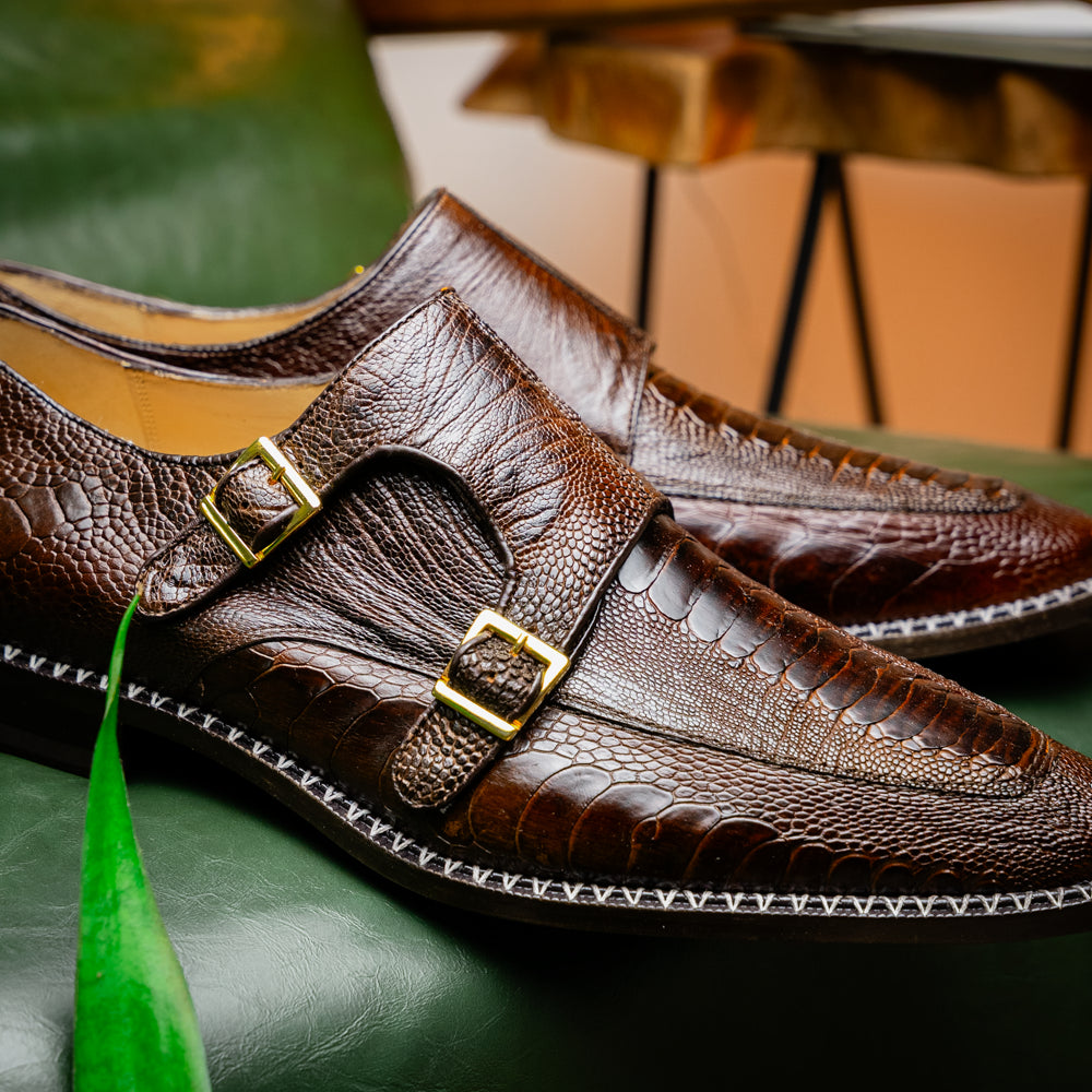 The Marco Di Milano Napoli Brown features brown leather double monk strap dress shoes with a genuine ostrich leg pattern and gold buckles, shown with one shoe upright and the other on its side.