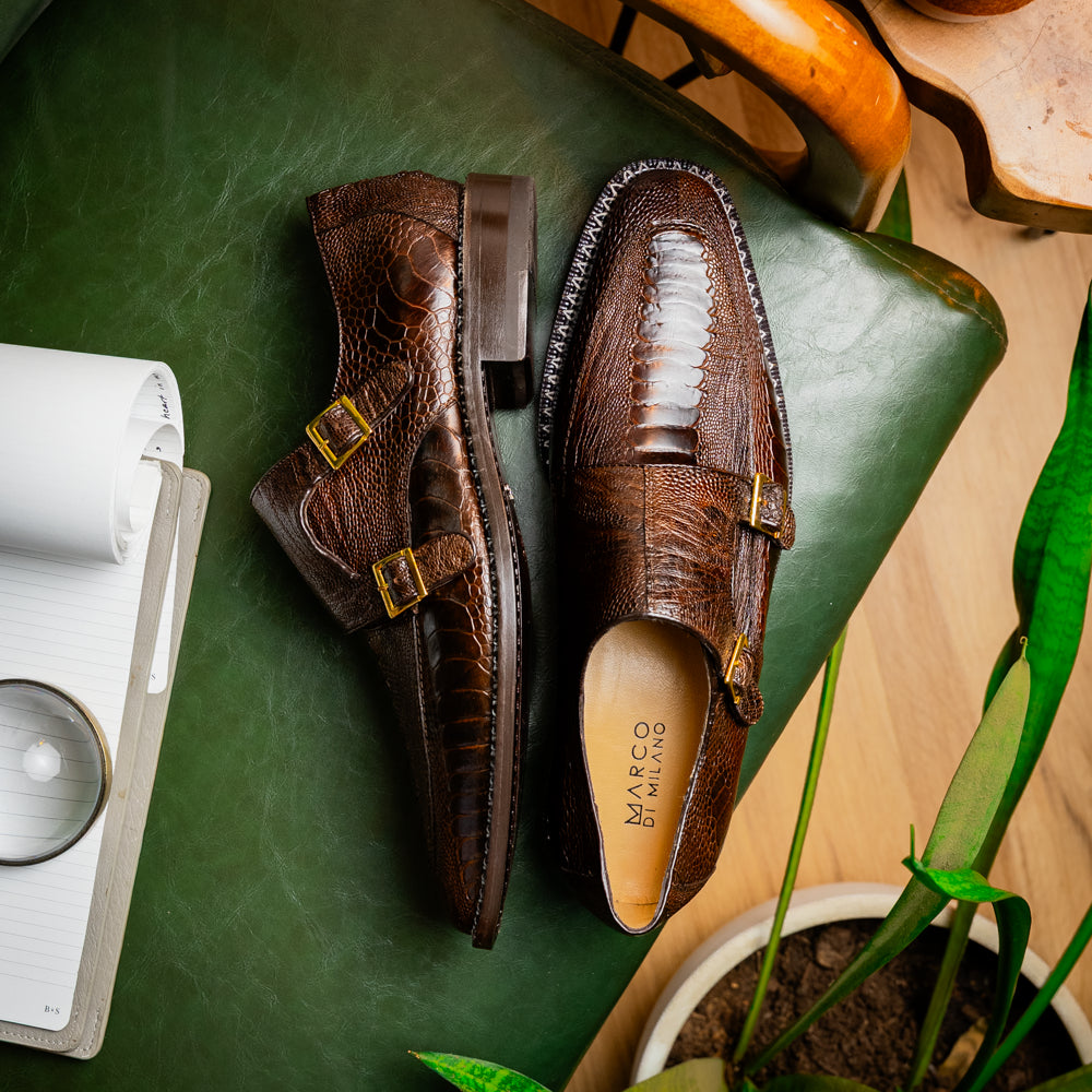 The Marco Di Milano Napoli Brown features brown leather double monk strap dress shoes with a genuine ostrich leg pattern and gold buckles, shown with one shoe upright and the other on its side.
