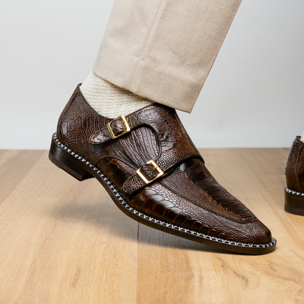 The Marco Di Milano Napoli Brown features brown leather double monk strap dress shoes with a genuine ostrich leg pattern and gold buckles, shown with one shoe upright and the other on its side.