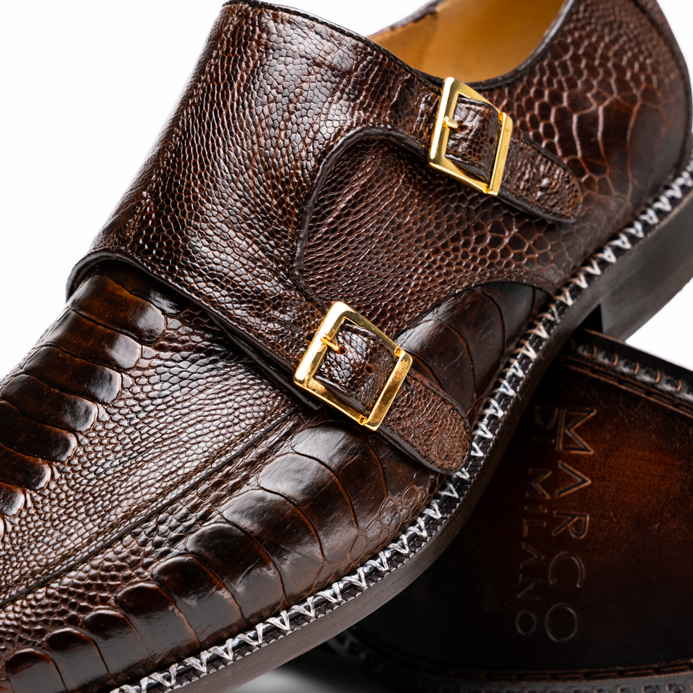 The Marco Di Milano Napoli Brown features brown leather double monk strap dress shoes with a genuine ostrich leg pattern and gold buckles, shown with one shoe upright and the other on its side.