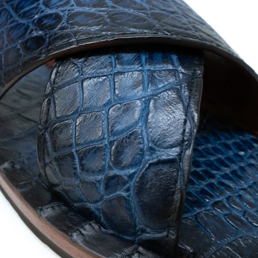 The Elios Navy by Marco Di Milano is a blue textured leather sandal with crisscross straps, a flat brown sole, and hand-painted finishes, shown on a white background.