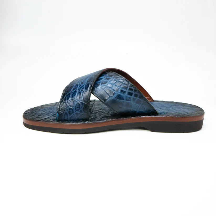 The Elios Navy by Marco Di Milano is a blue textured leather sandal with crisscross straps, a flat brown sole, and hand-painted finishes, shown on a white background.