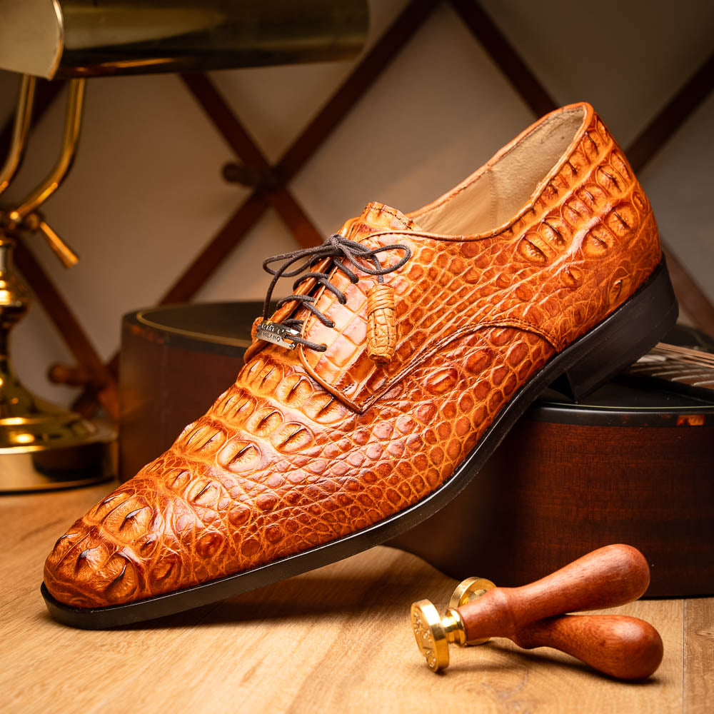The Nilo Brandy by Marco Di Milano is a pair of orange luxury shoes made from Premium Nile Crocodile Skin with black laces—one shoe upright, the other flat to highlight its exquisite sole.