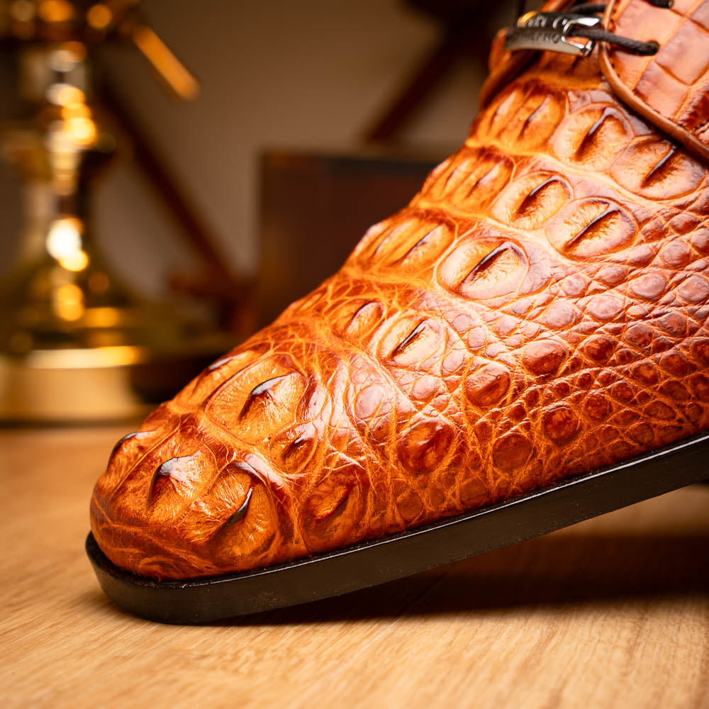 The Nilo Brandy by Marco Di Milano is a pair of orange luxury shoes made from Premium Nile Crocodile Skin with black laces—one shoe upright, the other flat to highlight its exquisite sole.