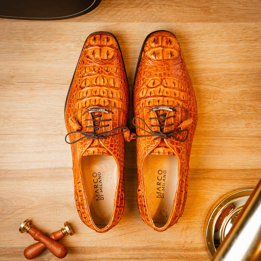 The Nilo Brandy by Marco Di Milano is a pair of orange luxury shoes made from Premium Nile Crocodile Skin with black laces—one shoe upright, the other flat to highlight its exquisite sole.