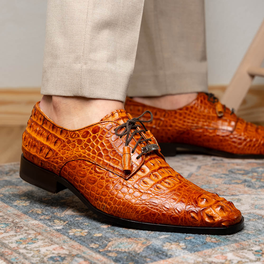 The Nilo Brandy by Marco Di Milano is a pair of orange luxury shoes made from Premium Nile Crocodile Skin with black laces—one shoe upright, the other flat to highlight its exquisite sole.