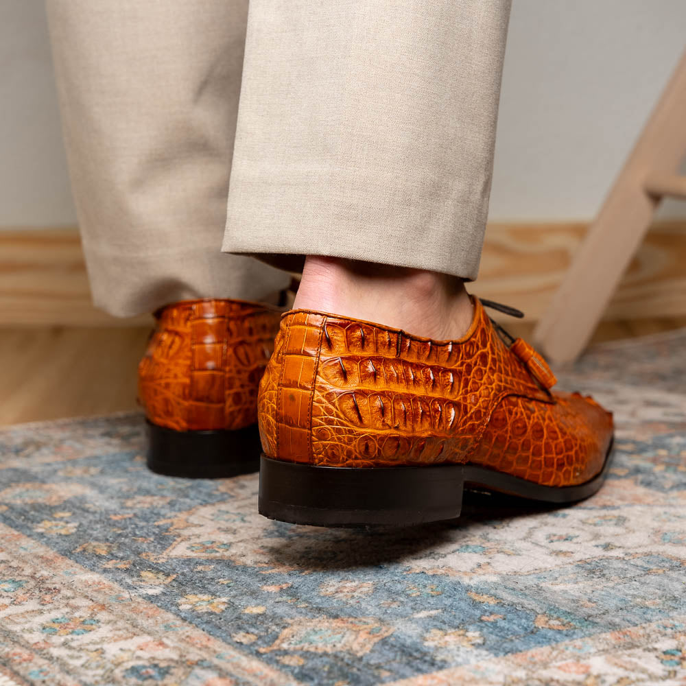 The Nilo Brandy by Marco Di Milano is a pair of orange luxury shoes made from Premium Nile Crocodile Skin with black laces—one shoe upright, the other flat to highlight its exquisite sole.