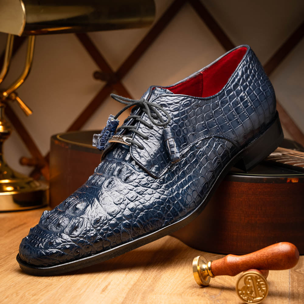 The Nilo Navy by Marco Di Milano features dark blue luxury footwear crafted from premium Nile crocodile skin with black laces and brown leather soles, displayed with one shoe propped on the other.