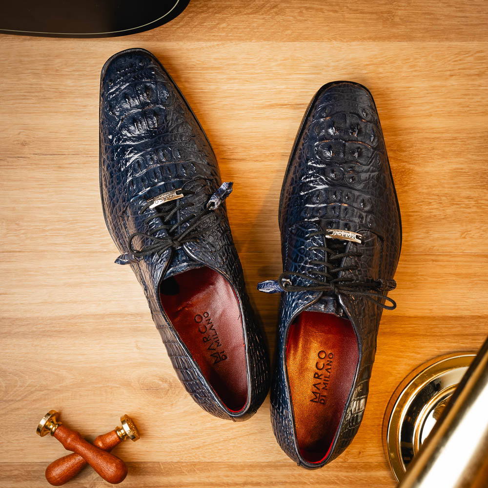 The Nilo Navy by Marco Di Milano features dark blue luxury footwear crafted from premium Nile crocodile skin with black laces and brown leather soles, displayed with one shoe propped on the other.