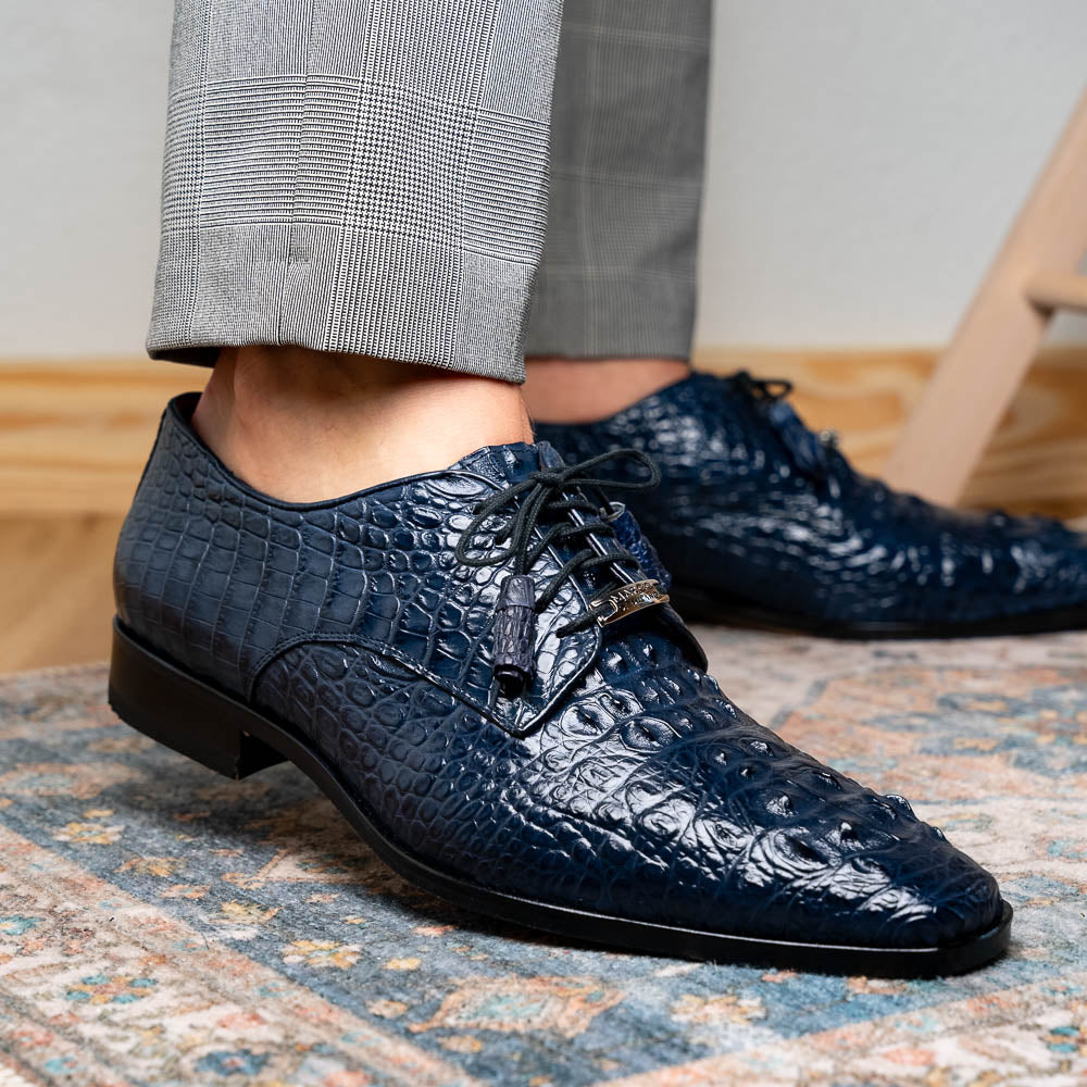 The Nilo Navy by Marco Di Milano features dark blue luxury footwear crafted from premium Nile crocodile skin with black laces and brown leather soles, displayed with one shoe propped on the other.