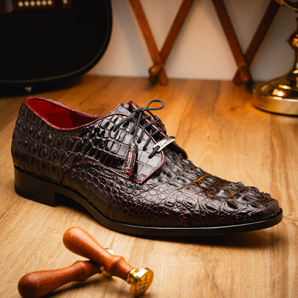 The Marco Di Milano Nilo Wine shoes are luxury dress footwear crafted from dark brown, textured Italian leather, featuring red interior lining and tan leather soles, with one shoe stylishly propped on the other.