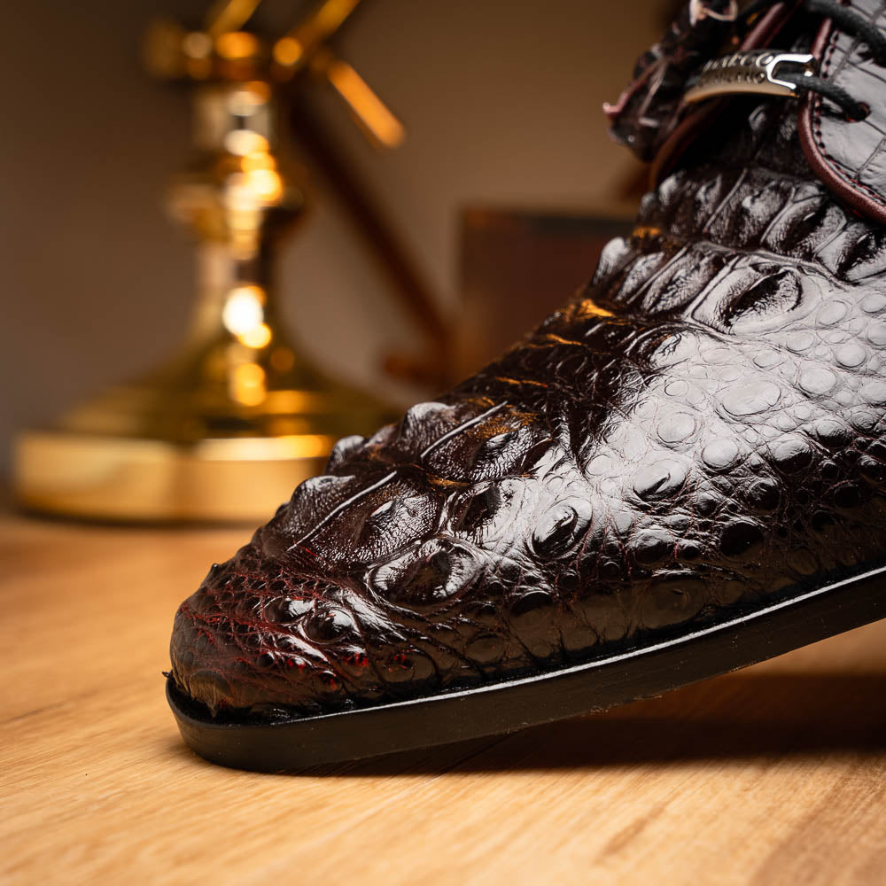The Marco Di Milano Nilo Wine shoes are luxury dress footwear crafted from dark brown, textured Italian leather, featuring red interior lining and tan leather soles, with one shoe stylishly propped on the other.